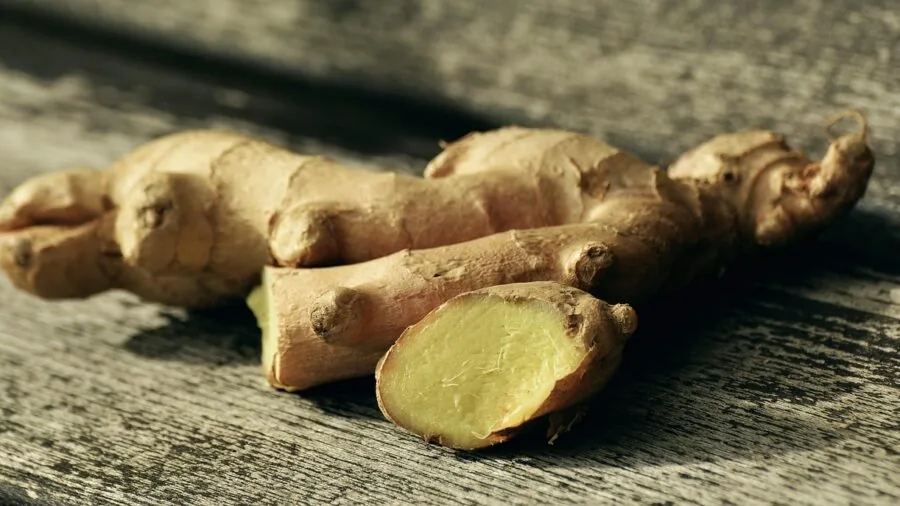 Close-up of fresh ginger root and golden turmeric powder on a wooden surface with natural lighting