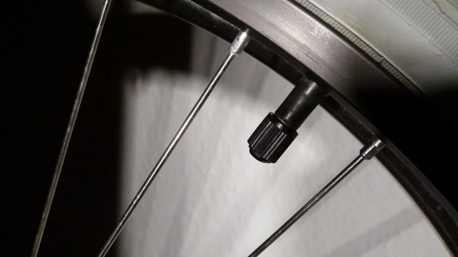 Close-up of hand inspecting a vehicle tire valve stem in natural daylight outdoors