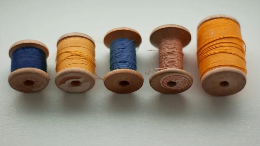 Close-up of hands adjusting thread tension on sewing machine with multiple thread spools visible