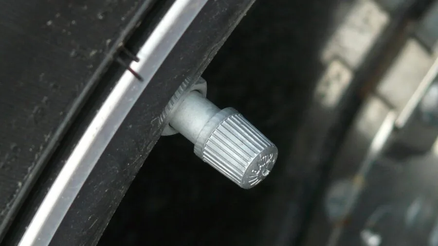 Close-up of hands installing a valve stem cap on a car tire during routine vehicle maintenance