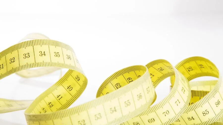 Close-up of hands measuring a hair dryer nozzle with a measuring tape on bathroom counter