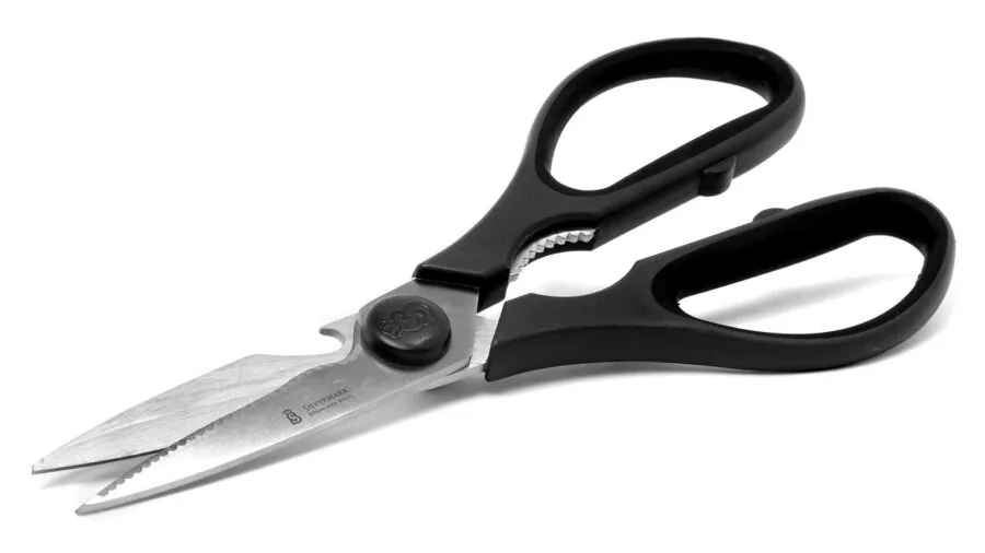 Close-up of hands using sharp fabric scissors to cut colorful textile material on work surface