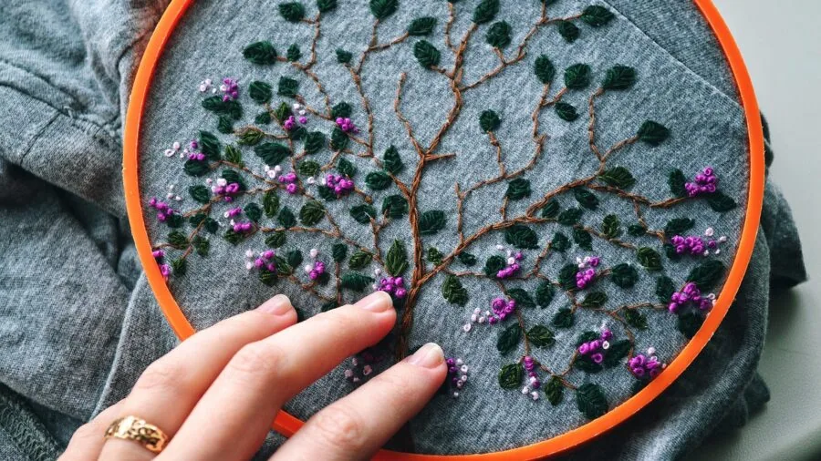 Close-up of hands working on cross stitch embroidery with visible stitches on fabric