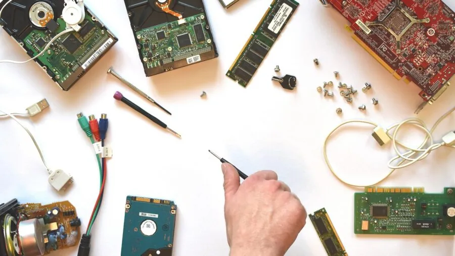 Close-up of hands working on delicate circuit board repair with tools and components on wooden workbench