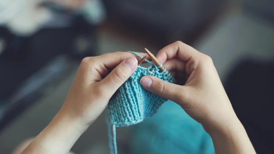 Close-up of hands working on intricate lace knitting project with fine yarn and needles