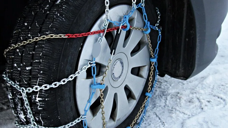 Close-up of metal snow chains wrapped around a vehicle tire on a snowy mountain road during winter driving conditions
