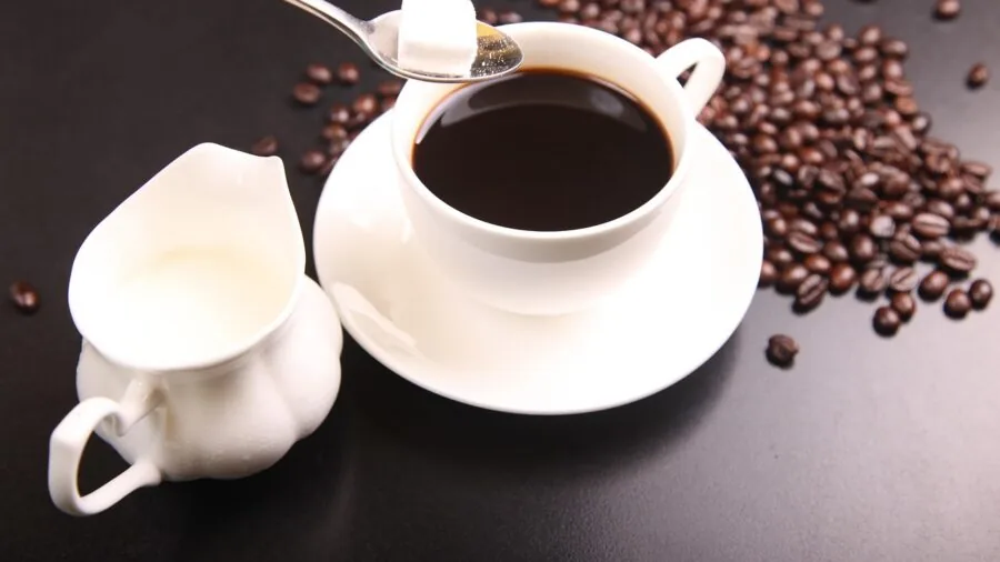 Close-up of rich milk being poured into a latte, creating foam and swirl patterns in warm coffee