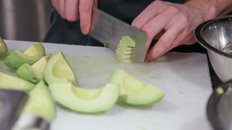 Close-up of sharp kitchen shears cutting fresh vegetables on a wooden cutting board in natural light