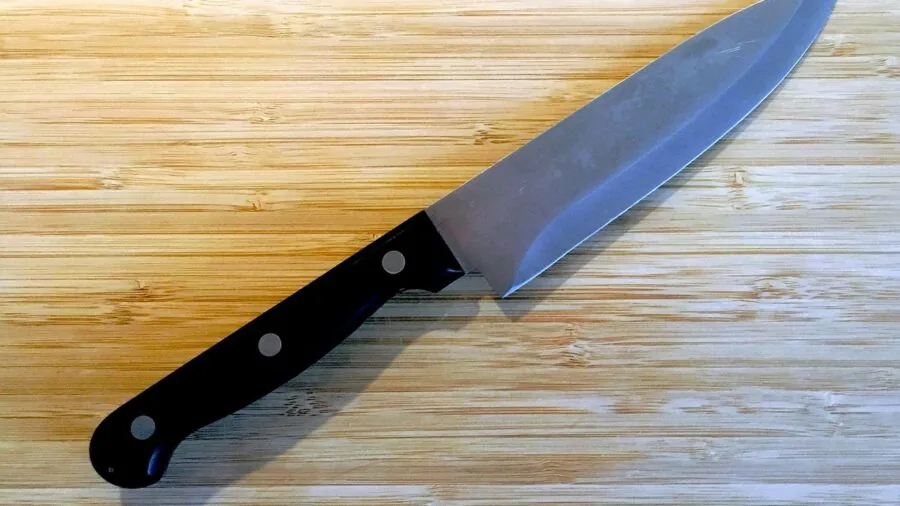Close-up of sharp knife blade during food preparation on wooden surface