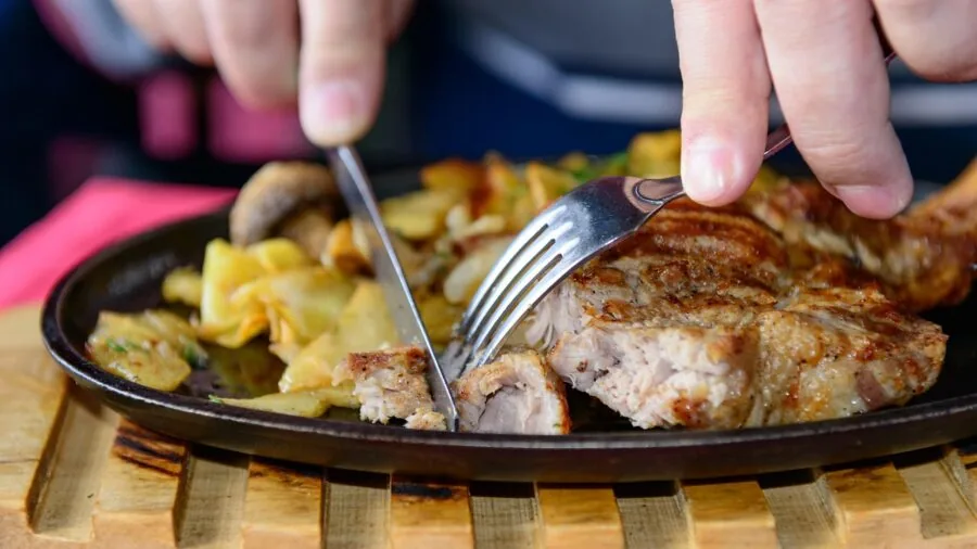 Close-up of someone using a serrated steak knife to cut meat during a dinner meal
