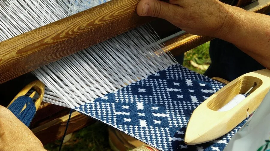 Close-up of weaver's hands threading vertical threads onto a wooden loom during the warping process