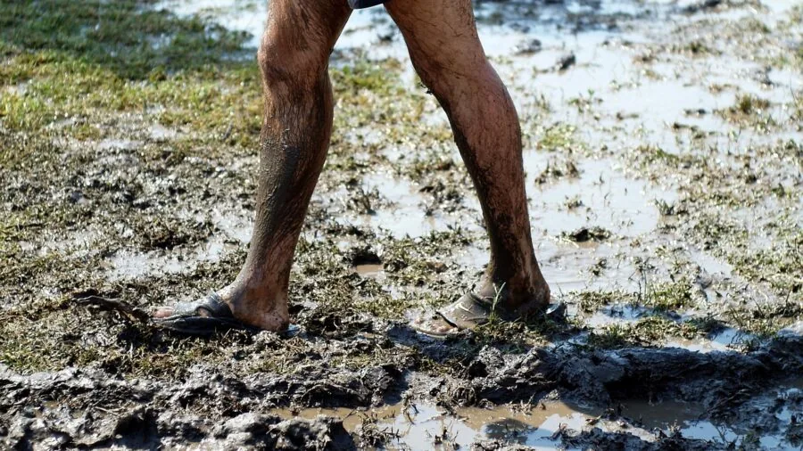 Close-up of wet hiking boots stepping through muddy water during outdoor trek through forest