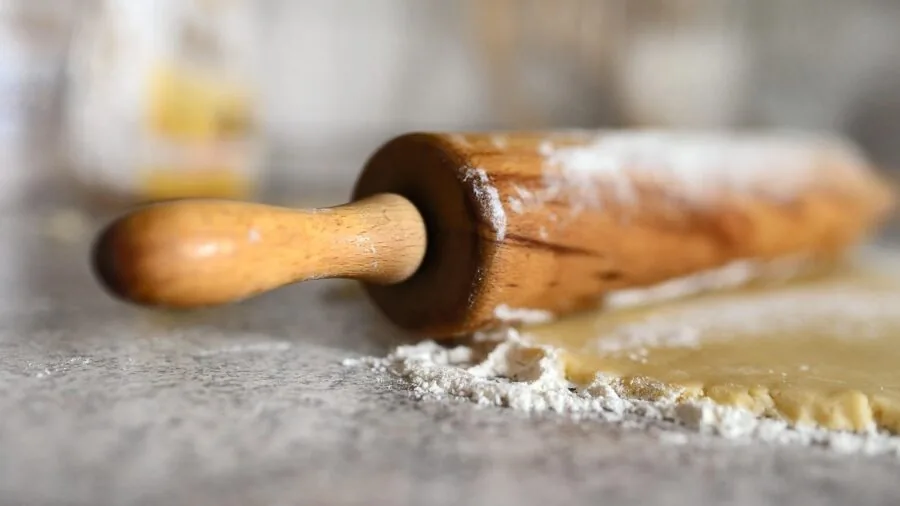 Close-up of wooden rolling pin with flour dusting on fresh dough during home baking preparation