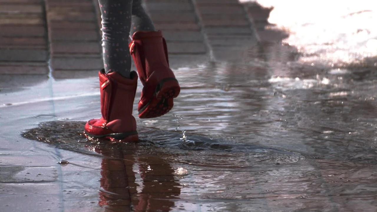 Colorful rain boots standing in puddle on wet ground