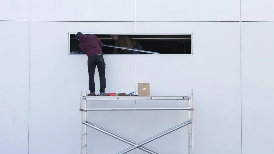 Construction worker in safety gear climbing ladder while carrying tools and equipment on job site