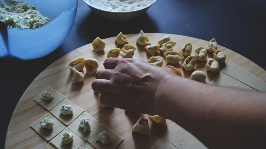 Cook grating fresh cheese over pasta in a bright, home kitchen setting