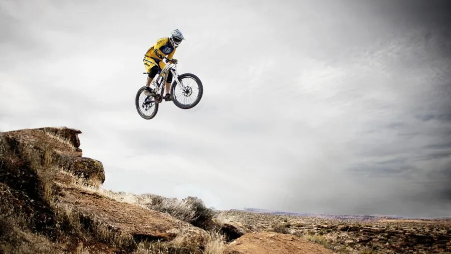 Cyclist riding a gravel bike on a dusty mountain trail with scenic landscape backdrop