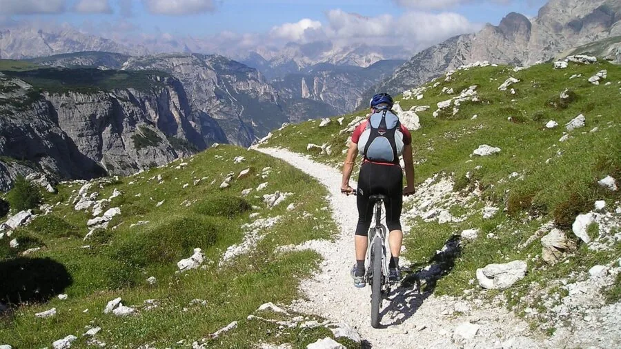 Cyclist riding fully loaded touring bike on scenic mountain road with gear packed for long journey