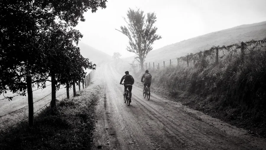 Cyclist riding gravel bike on dusty trail through natural landscape with bikepacking gear