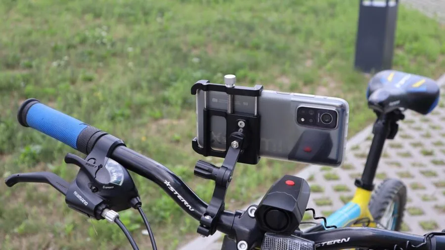 Cyclist struggling with phone mount setup on handlebars during outdoor ride