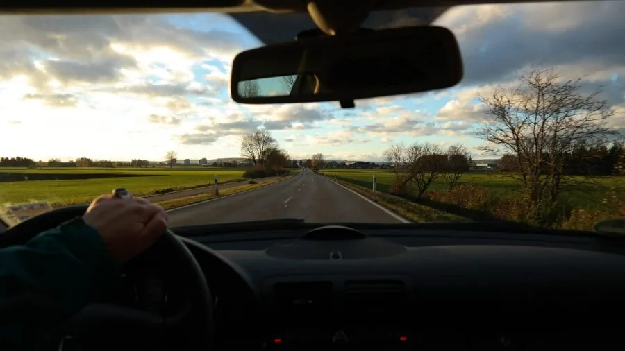 Driver's hand on steering wheel while operating car dashboard controls safely during daytime driving