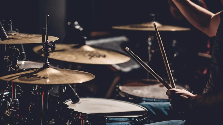 Drummer performing with cymbals during live music session, showing instrument details and playing technique