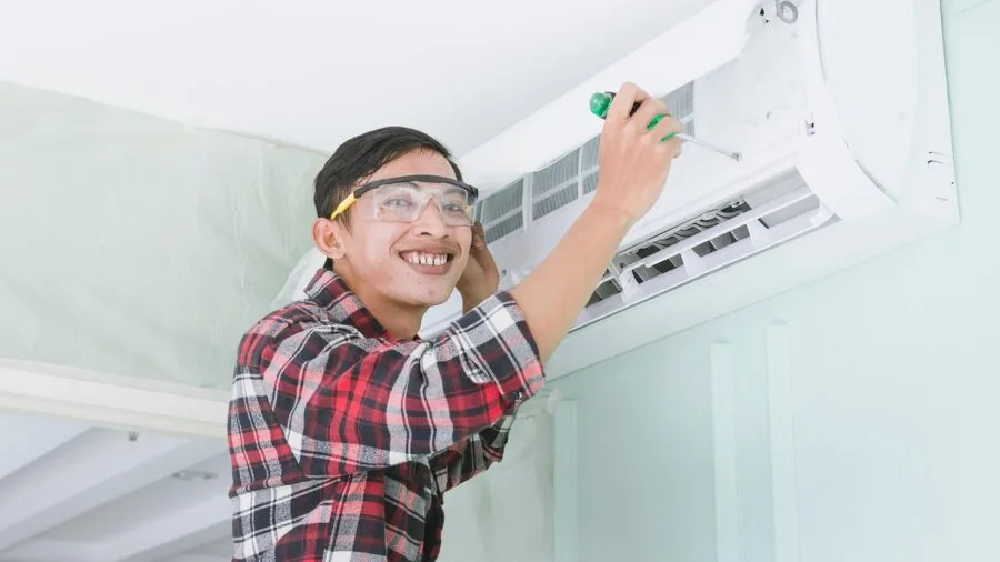 Electrician accessing and servicing mounted electrical equipment on interior wall for maintenance
