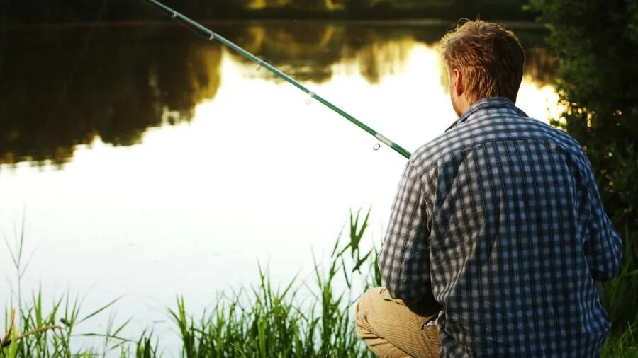 Experienced fisherman casting rod into calm lake water during golden hour sunrise