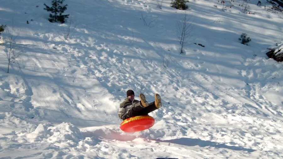 Family enjoying winter sledding together on snowy hillside during daytime