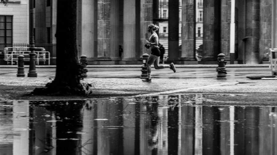 Female jogger outdoors checking phone on running belt while exercising on city street