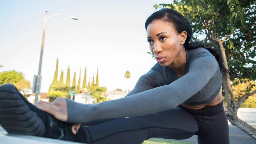 Female runner stretching legs on outdoor path, demonstrating range of motion and athletic flexibility