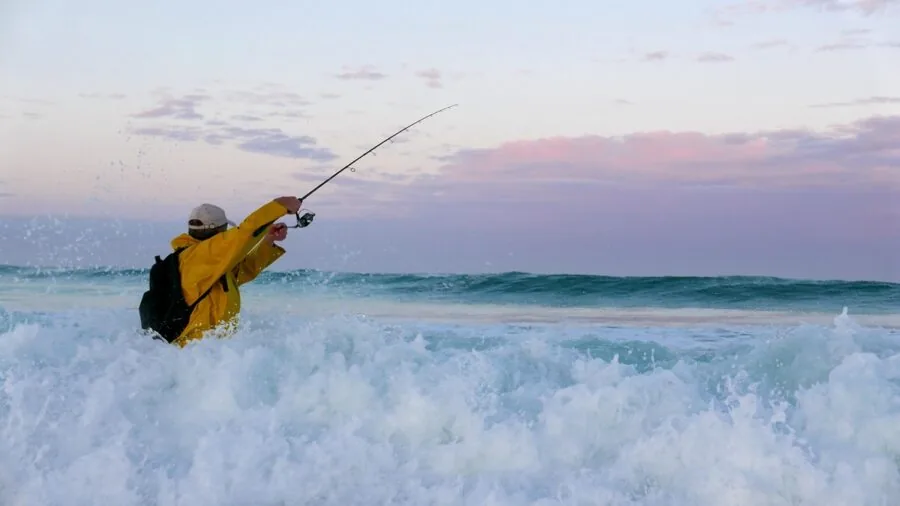 Fisherman casting line in rocky coastal saltwater environment during daytime
