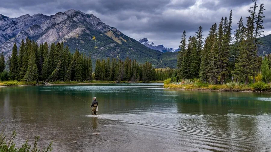 Fisherman casting line in rocky river with natural landscape and flowing water