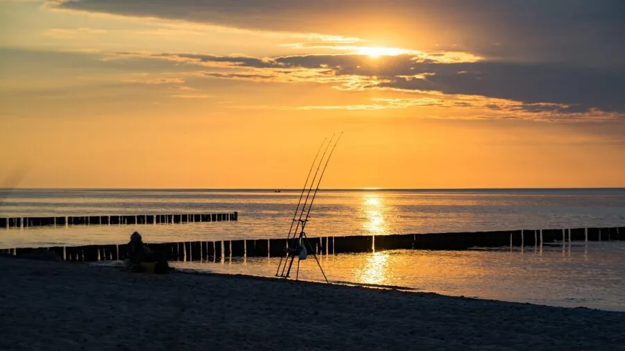 Fisherman casting line on calm water with sunlight reflection demonstrating lens visibility and water conditions