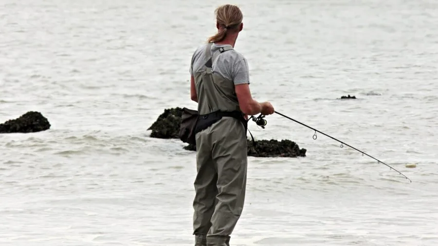 Fisherman casting spinning rod with line tension over calm water