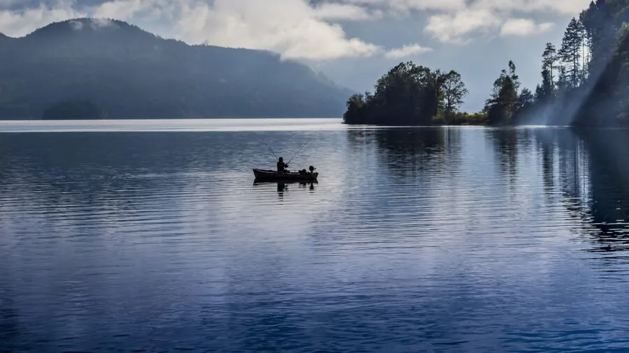 Fisherman selecting equipment by riverbank, contemplating gear choice for fishing trip