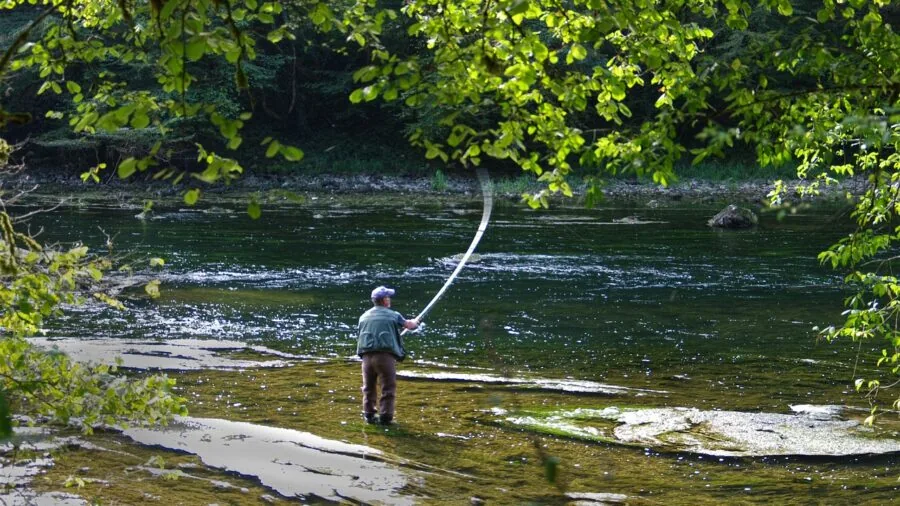 Fly fisherman examining rod equipment by riverside, representing product quality and brand confidence