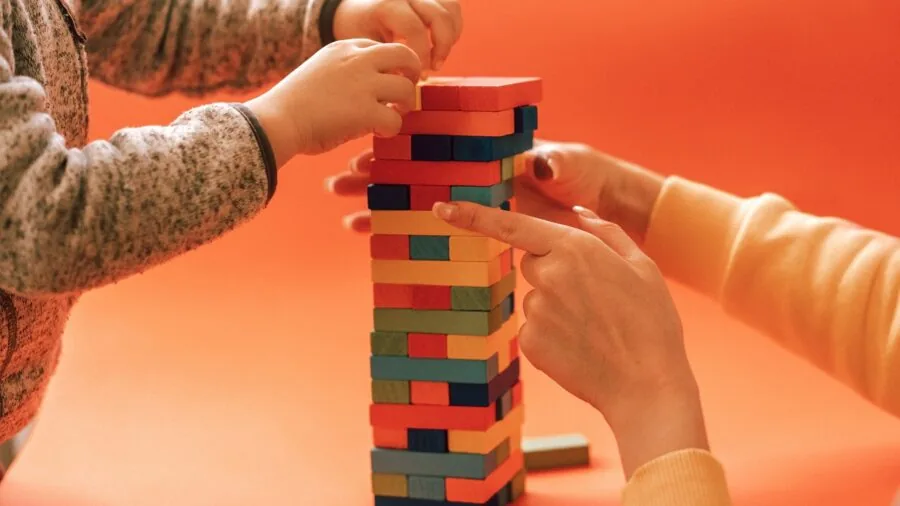 Friends playing wooden block stacking game outdoors on grass during sunny day