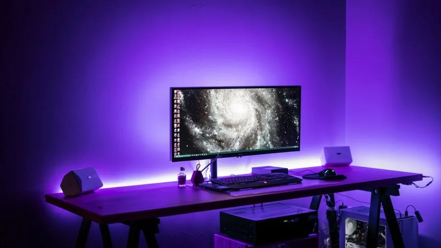 Gamer's desk with vibrant RGB lighting illuminating keyboard and gaming setup in dark room