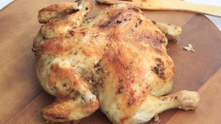 Golden roasted chicken with crispy skin on a baking sheet in a warm kitchen setting