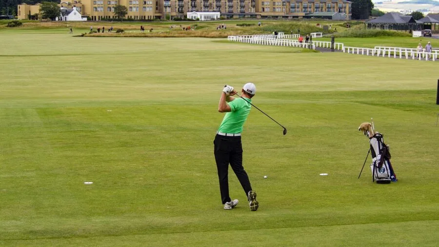 Golfer executing a driver swing on a sunny golf course with trees in background