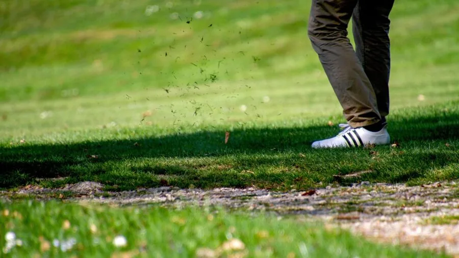 Golfer in sunglasses measuring distance to flag on scenic golf course fairway