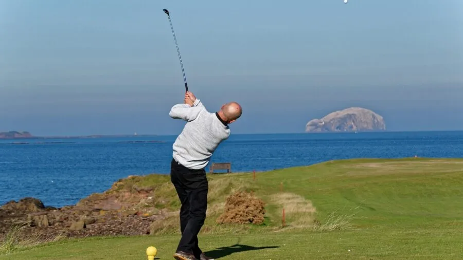 Golfer mid-swing with driver on fairway during sunny day
