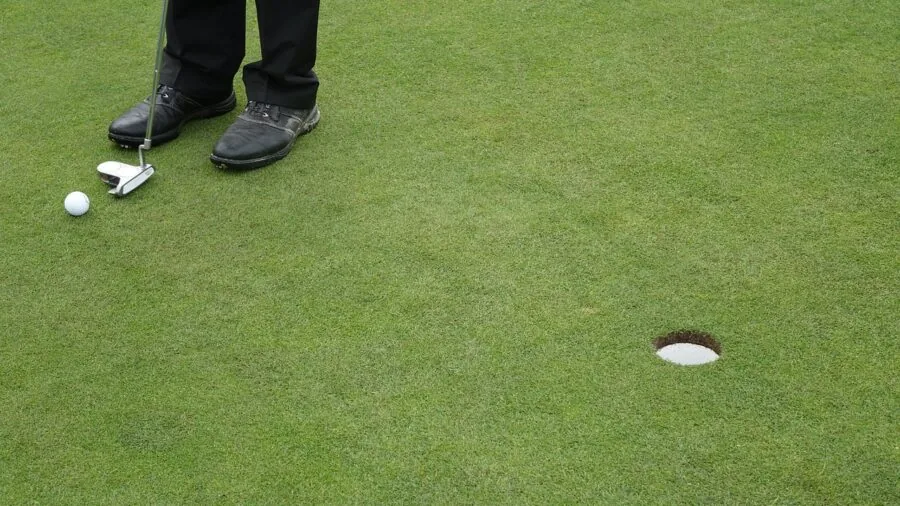 Golfer practicing putting stroke on indoor green mat with focused concentration