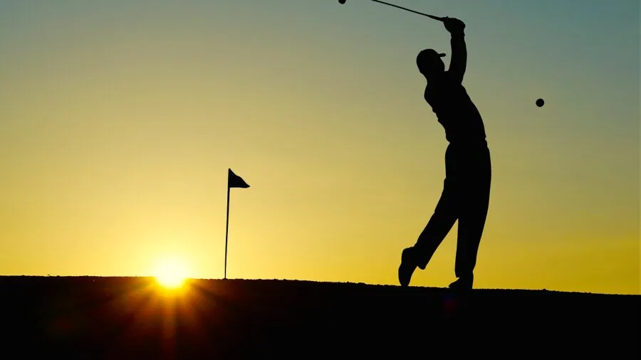 Golfer practicing swing on hitting mat in backyard during daytime
