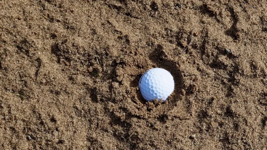 Golfer stretching to retrieve ball from water hazard on golf course