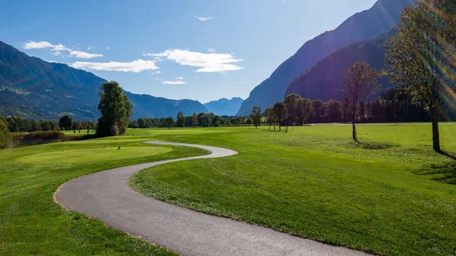 Golfer walking across golf course fairway during sunny day with golf bag
