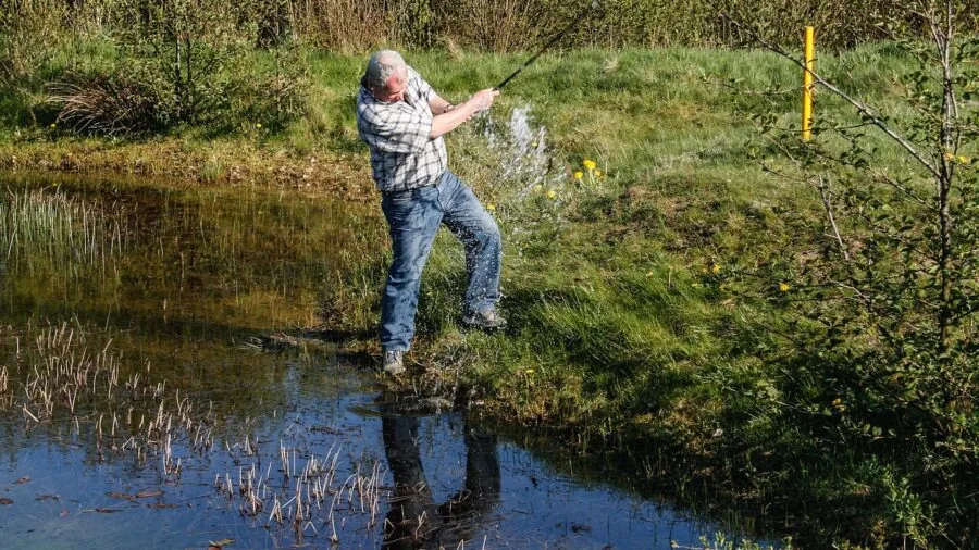Golfer with wet hands retrieving golf ball from water hazard on course