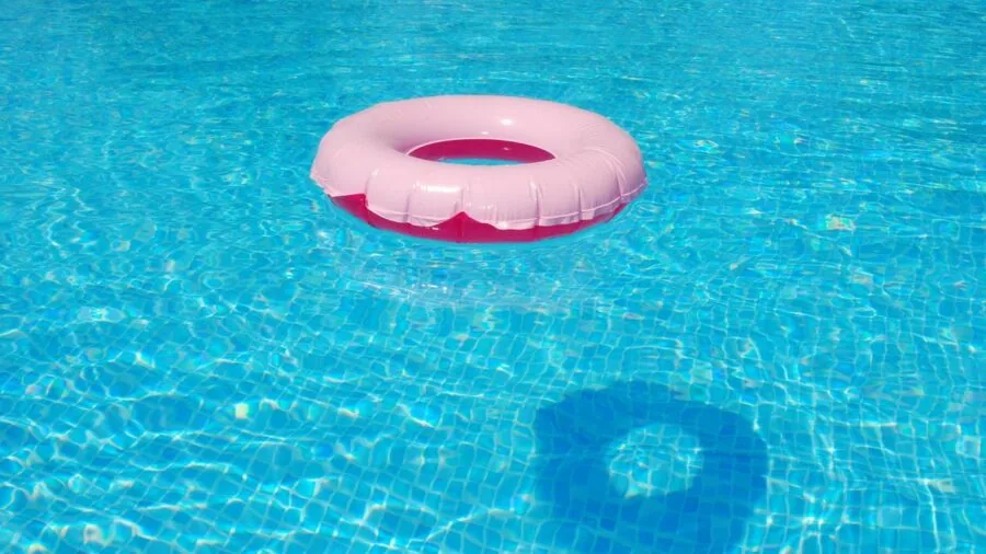 Group of friends enjoying various pool floats and loungers in a swimming pool on a sunny day