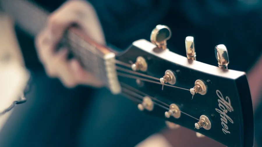 Guitarist adjusting tuning pegs on acoustic guitar during practice session